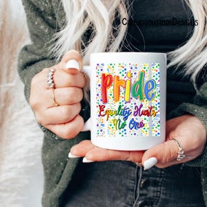 May include: White ceramic mug featuring the word "Pride" in rainbow colors, with the phrase "Equality Hurts No One." The mug has a colorful confetti pattern and vertical stripes. The mug is held by a person.