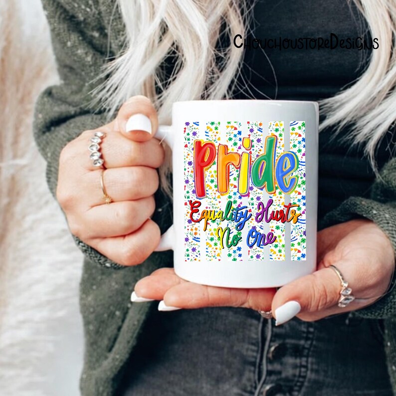 May include: White ceramic mug featuring the word "Pride" in rainbow colors, with the phrase "Equality Hurts No One." The mug has a colorful confetti pattern and vertical stripes. The mug is held by a person.