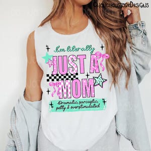 May include: White sleeveless shirt with the text "I'm literally JUST A MOM" in pink, with decorative stars and bows. The shirt also includes the phrase "Dramatic, sarcastic, petty & overstimulated".
