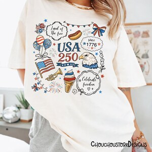 Puede incluir: Camiseta color crema con un dise&ntilde;o gr&aacute;fico colorido que celebra el 250 aniversario de los Estados Unidos. El dise&ntilde;o incluye una bandera estadounidense, un &aacute;guila, fuegos artificiales y el texto "Land of the free" y "Celebrate freedom".
