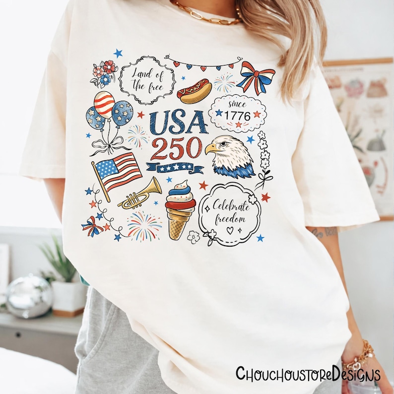 Puede incluir: Camiseta color crema con un dise&ntilde;o gr&aacute;fico colorido que celebra el 250 aniversario de los Estados Unidos. El dise&ntilde;o incluye una bandera estadounidense, un &aacute;guila, fuegos artificiales y el texto "Land of the free" y "Celebrate freedom".