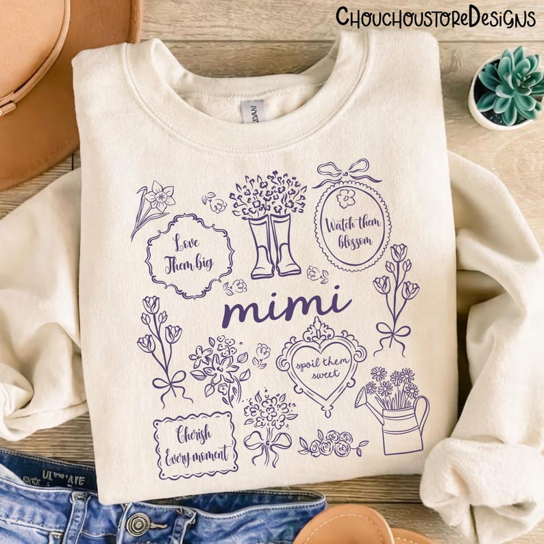 May include: Cream-colored sweatshirt with a purple floral design and the word "mimi". The design includes boots, flowers, and phrases like "Love them big" and "Cherish every moment". The brand name "Chouchoustore Designs" is at the top.