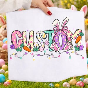 May include: White Easter-themed towel with the word "CUSTOM" in colorful, patterned letters. The design includes bunny ears, carrots, Easter eggs, and paw prints. A string of lights with flowers and eggs decorates the bottom.