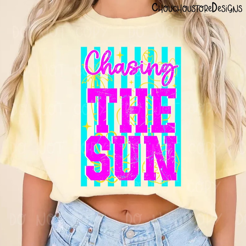May include: A light yellow t-shirt with the text "Chasing The Sun" in bright pink, set against a turquoise striped background. The shirt is a casual style, suitable for warm weather.