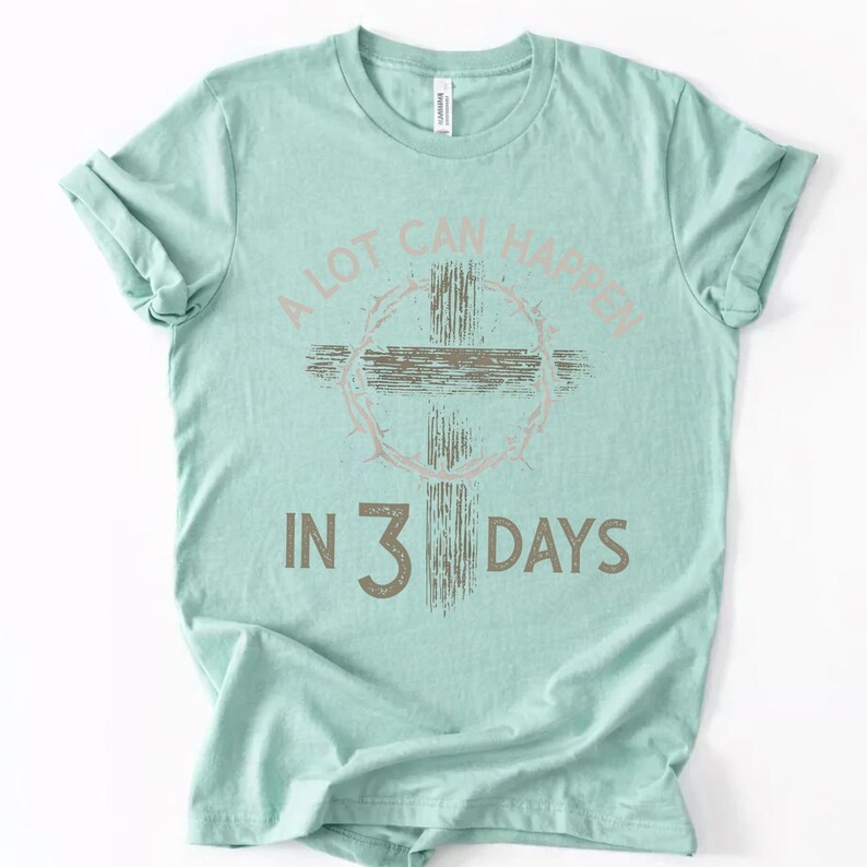 Puede incluir: Camiseta verde claro con el texto "A LOT CAN HAPPEN IN 3 DAYS". El dise&ntilde;o incluye una cruz y una corona de espinas en tonos rosa y marr&oacute;n apagados. El texto est&aacute; en una fuente desgastada.