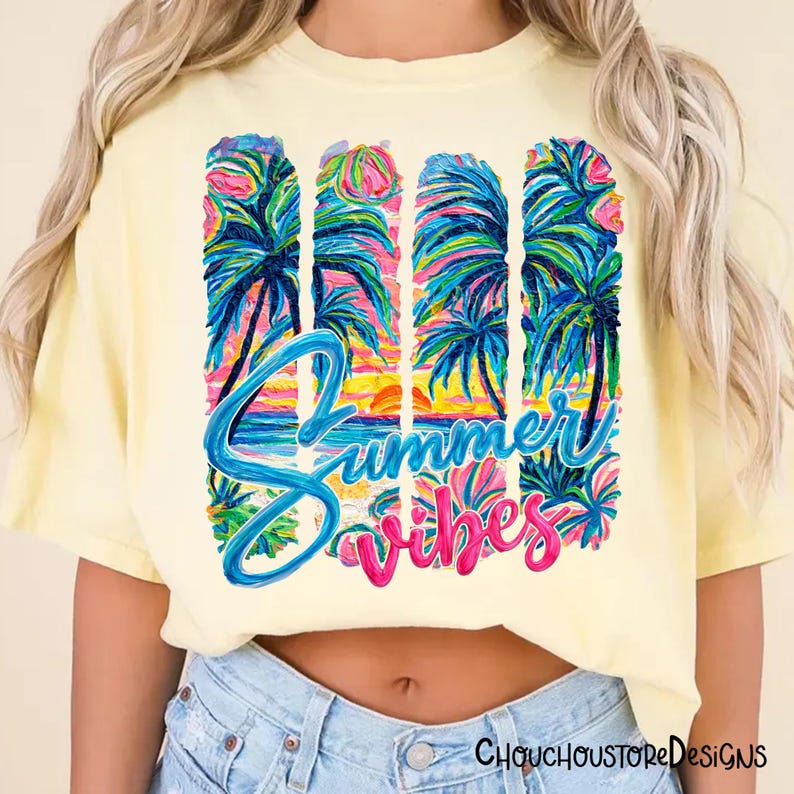 May include: A light yellow t-shirt with a colorful tropical design. The design features palm trees, a sunset, and the words "Summer Vibes" in blue and pink script. The shirt is a casual, relaxed fit.