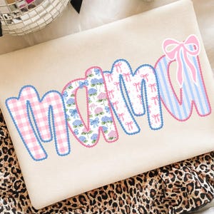 May include: A beige sweatshirt with the word "mama" in a patchwork design. The letters feature pink gingham, floral patterns, and blue and pink striped fabric, all outlined in blue and pink scalloped trim.
