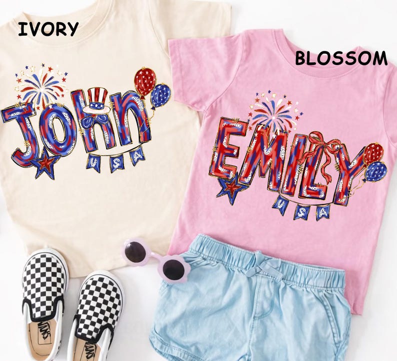 Puede incluir: Dos camisetas infantiles, una marfil y otra rosa, con nombres personalizados en rojo, blanco y azul. La camiseta marfil dice "John" y la rosa "Emily". Ambas camisetas tienen gr&aacute;ficos festivos y la palabra "USA".