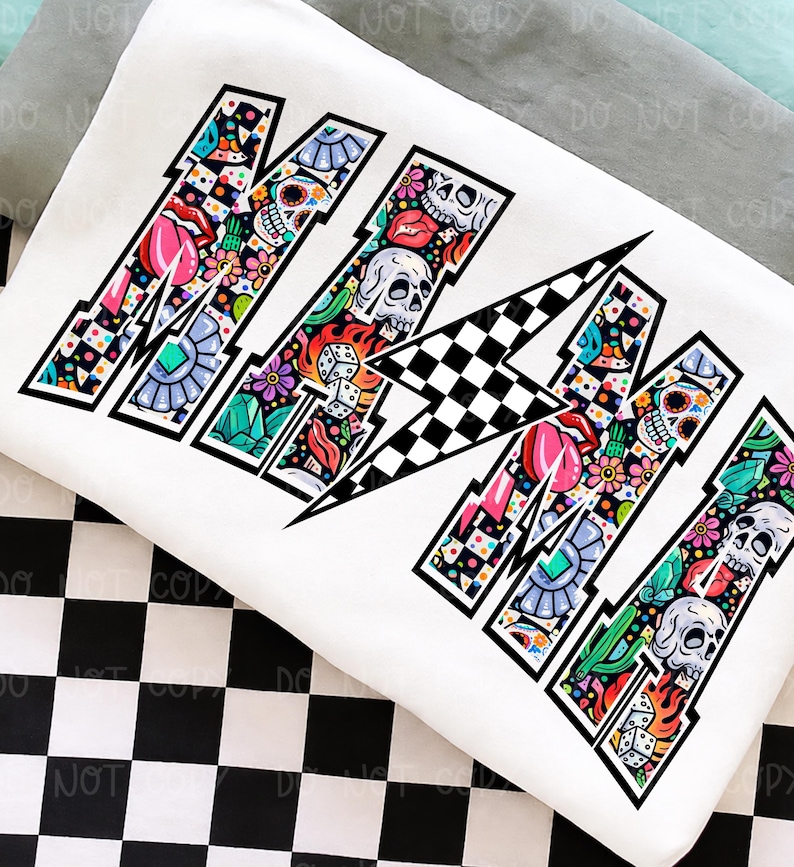 May include: White sweatshirt with the word "MAMA" in a bold, stylized font. Each letter is filled with colorful illustrations including skulls, flowers, dice, and lips. The design has a black outline and a checkered pattern.