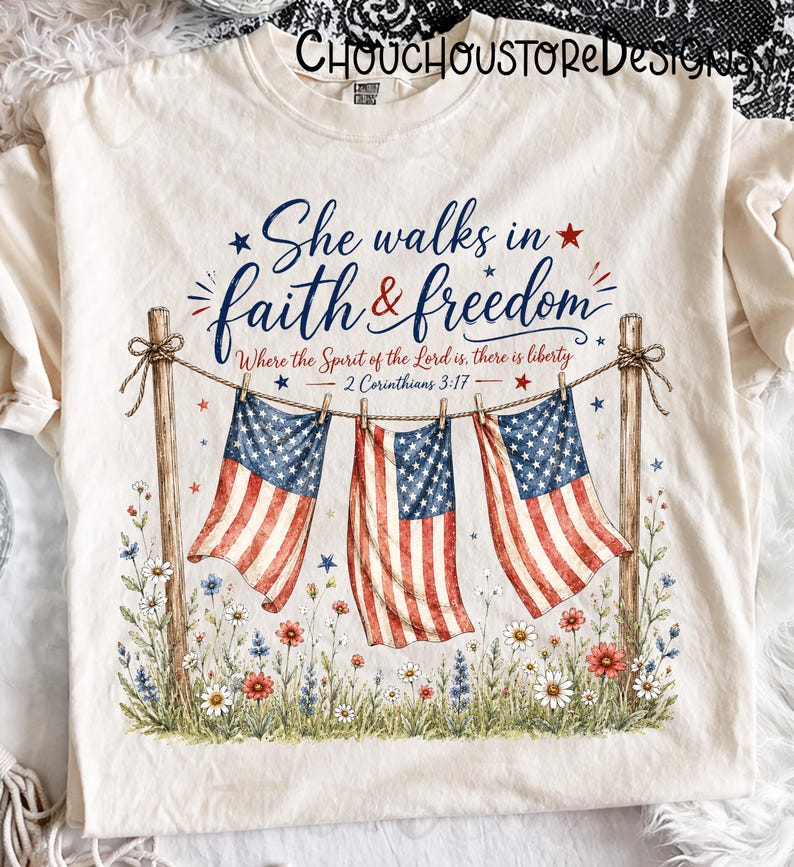 May include: Cream-colored t-shirt featuring the text "She walks in faith & freedom" with American flags and floral accents. The design includes the Bible verse 2 Corinthians 3:17. A patriotic and inspirational graphic tee.