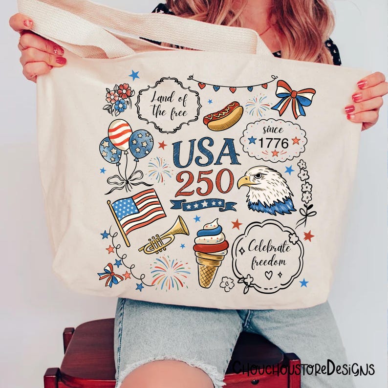 Puede incluir: Bolso tote color crema con ilustraciones patri&oacute;ticas. El dise&ntilde;o incluye una bandera estadounidense ondeando, globos, fuegos artificiales, un perrito caliente y un helado. El texto incluye "USA 250" y "Celebra la libertad."