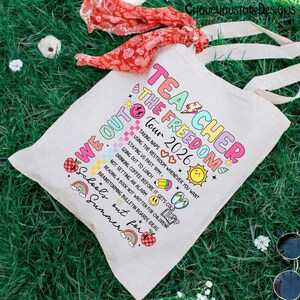 May include: A white canvas tote bag with the text "Teacher The Freedom Tour 2026" in colorful letters. The bag features a list of fun summer activities. A red scarf and sunglasses are on the green grass.