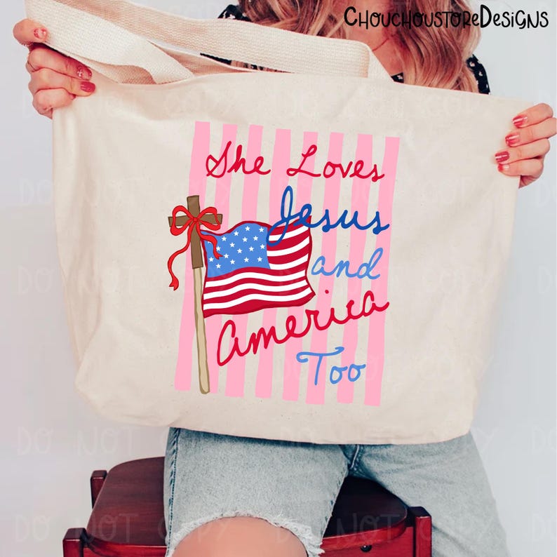 May include: Cream-colored tote bag with the text "She Loves Jesus and America Too" in red and blue script. The design includes a waving American flag and pink vertical stripes.