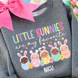 May include: A gray sweatshirt with the text "LITTLE BUNNIES are my favorite" in colorful letters. Below are five cartoon bunnies in different colored outfits, each holding an Easter egg. The word "NICU" is printed at the bottom.