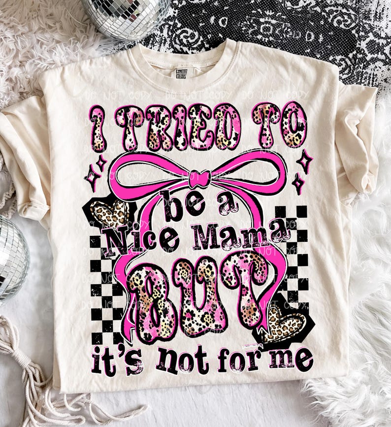 May include: Cream-colored t-shirt with the text "I tried to be a Nice Mama BUT it's not for me" in pink and leopard print. The design includes a pink bow, stars, and a checkered pattern.