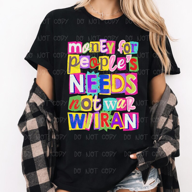 May include: Black t-shirt with the text "money for people's NEEDS not war WIRAN" in colorful block letters. The shirt is worn with a black and gray plaid shirt.