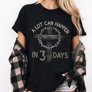Puede incluir: Camiseta negra con el texto "A LOT CAN HAPPEN IN 3 DAYS" en una fuente desgastada. El dise&ntilde;o presenta una cruz y una corona de espinas. La camiseta es de estilo cuello redondo cl&aacute;sico.