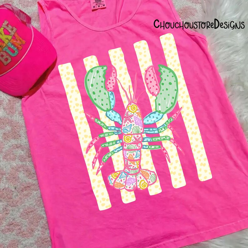 May include: A bright pink tank top with a colorful lobster graphic and vertical stripes. A matching pink baseball cap with the text "KE BUM" is visible in the upper left corner. The tank top features a scoop neck.
