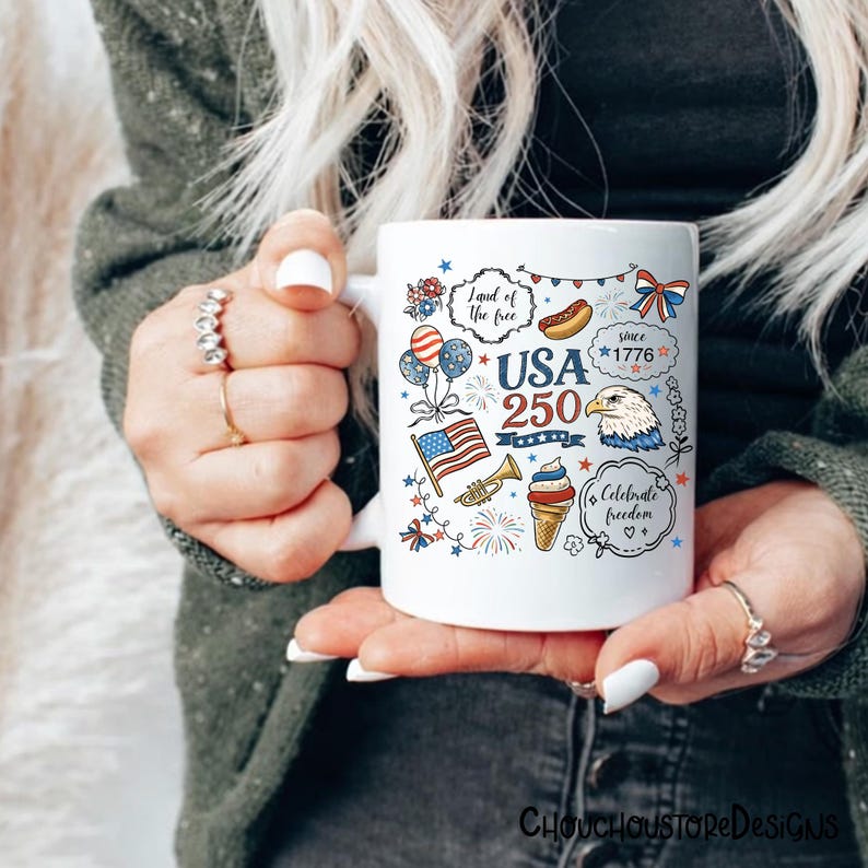 Puede incluir: Taza de cer&aacute;mica blanca con ilustraciones patri&oacute;ticas y texto. El dise&ntilde;o incluye la bandera estadounidense, un &aacute;guila, fuegos artificiales y las palabras "USA 250" y "Celebrate freedom". La taza es sostenida por una persona.