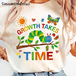 Puede incluir: Camiseta color crema con un gr&aacute;fico colorido que presenta una oruga, una mariposa y las palabras "GROWTH TAKES TIME". El dise&ntilde;o incluye un sol, corazones, piezas de rompecabezas y fruta. La marca "CHOUCHOUSTOREDESIGNS" est&aacute; en la parte superior.