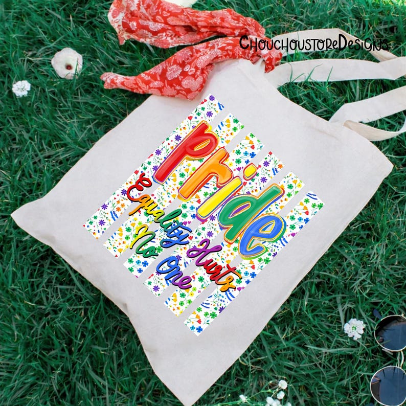 May include: A white tote bag with the words "Pride, Equality Hurts No One" in rainbow colors. The text is set against a background of colorful floral stripes. The bag has long white handles.