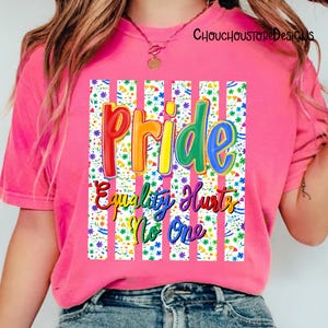 May include: A pink t-shirt with the word "Pride" in rainbow colors, and the phrase "Equality Hurts No One". The design is set against a floral pattern with white vertical stripes. The shirt is a casual wear item.
