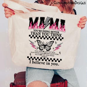 May include: Beige tote bag with the word "MAMA" in black with pink flames and a checkered lightning bolt. The bag has a butterfly graphic and the text "YOU'RE DOING BETTER THAN YOU THINK" and "I believe in you."