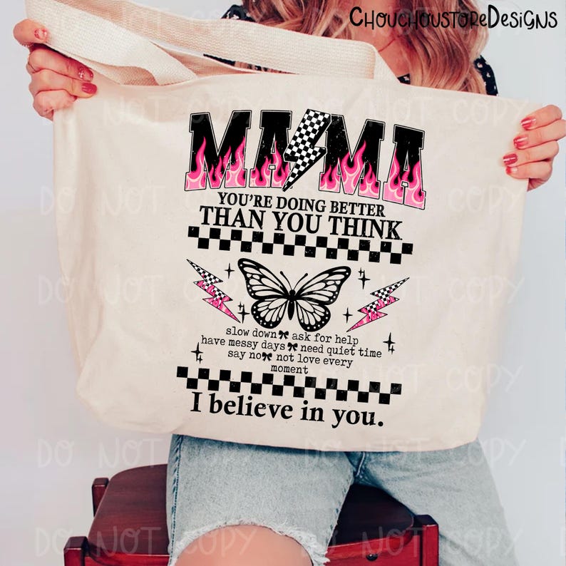 May include: Beige tote bag with the word "MAMA" in black with pink flames and a checkered lightning bolt. The bag has a butterfly graphic and the text "YOU'RE DOING BETTER THAN YOU THINK" and "I believe in you."