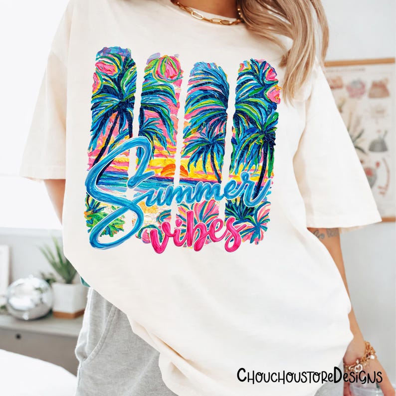 May include: Cream-colored t-shirt with a colorful graphic. The graphic features palm trees, a sunset, and the words "Summer Vibes" in blue and pink. The shirt is a casual, relaxed fit.