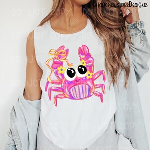 May include: White sleeveless shirt featuring a cartoon crab design. The crab is primarily pink with yellow and purple accents, large black eyes, and a smiling face. The crab's claws are adorned with yellow flowers and a yellow bow.