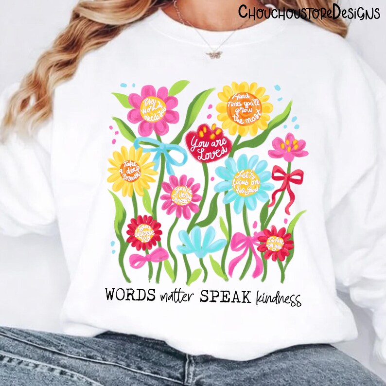 May include: White sweatshirt featuring a colorful floral design with inspirational quotes. The flowers are in shades of pink, yellow, and blue, with green leaves and bows. The text "WORDS matter SPEAK kindness" is at the bottom.