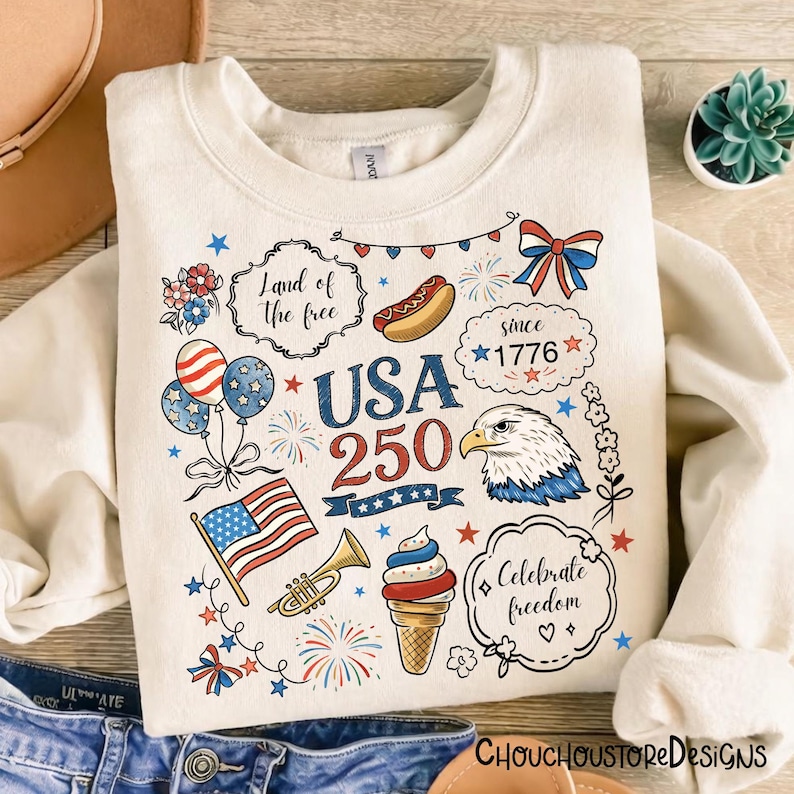Puede incluir: Sudadera de color crema con gr&aacute;ficos patri&oacute;ticos con tem&aacute;tica de EE. UU. Presenta el texto "USA 250" e ilustraciones de un perrito caliente, un helado, la bandera estadounidense, un &aacute;guila y fuegos artificiales. Incluye las frases "Land of the free" y "Celebrate freedom."