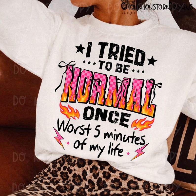 May include: White sweatshirt with the text "I TRIED TO BE NORMAL ONCE Worst 5 minutes of my life." The word "NORMAL" is in pink checkered letters with orange flames. Black stars and pink lightning bolts accent the text.