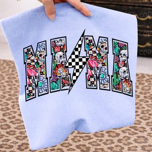 May include: A light blue sweatshirt with the word "MAMA" in a bold, colorful design. The letters are filled with skulls, flowers, and other graphics. A black and white checkered lightning bolt is in the center.
