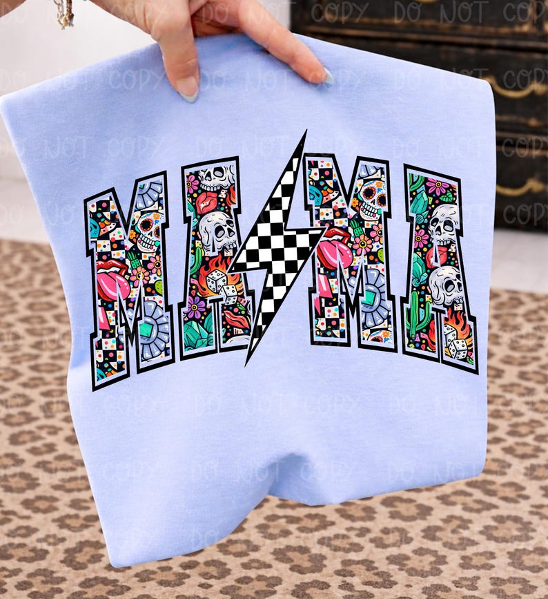 May include: A light blue sweatshirt with the word "MAMA" in a bold, colorful design. The letters are filled with skulls, flowers, and other graphics. A black and white checkered lightning bolt is in the center.