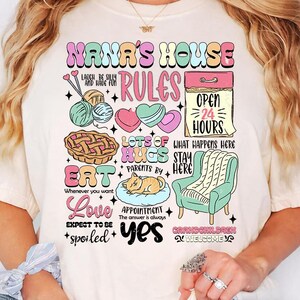 May include: Cream-colored t-shirt with a colorful graphic design. The design includes the text "NANA'S HOUSE RULES" with illustrations of yarn, hearts, a pie, a cat, and a chair. Additional text includes "Eat", "Love", and "Grandchildren Welcome".