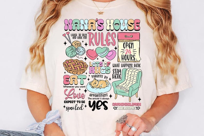 May include: Cream-colored t-shirt with a colorful graphic design. The design includes the text "NANA'S HOUSE RULES" with illustrations of yarn, hearts, a pie, a cat, and a chair. Additional text includes "Eat", "Love", and "Grandchildren Welcome".