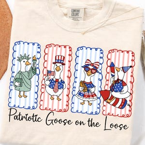 May include: Cream-colored t-shirt featuring four cartoon geese in patriotic attire. Each goose is in a rectangular frame with red and blue accents. The text "Patriotic Goose on the Loose" is printed below the geese.