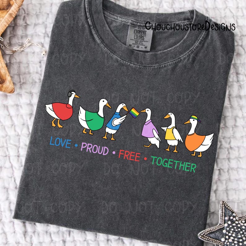 May include: Dark gray t-shirt featuring a line of cartoon ducks, each with unique outfits and accessories. The ducks are in various colors, and the text "LOVE &bull; PROUD &bull; FREE &bull; TOGETHER" is printed below them in rainbow colors.