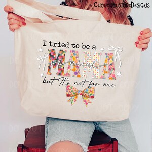 May include: A cream-colored tote bag with the text "I tried to be a nicer MAMA but It's not for me." The word "MAMA" is decorated with a floral pattern. The bag has a floral bow design at the bottom.