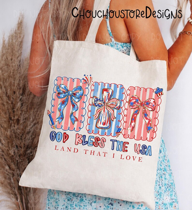 May include: A cream-colored tote bag featuring patriotic designs. The bag displays three framed images with red, white, and blue bows, a cross, and the text "GOD BLESS THE USA, LAND THAT I LOVE". The bag has a simple, rectangular shape.
