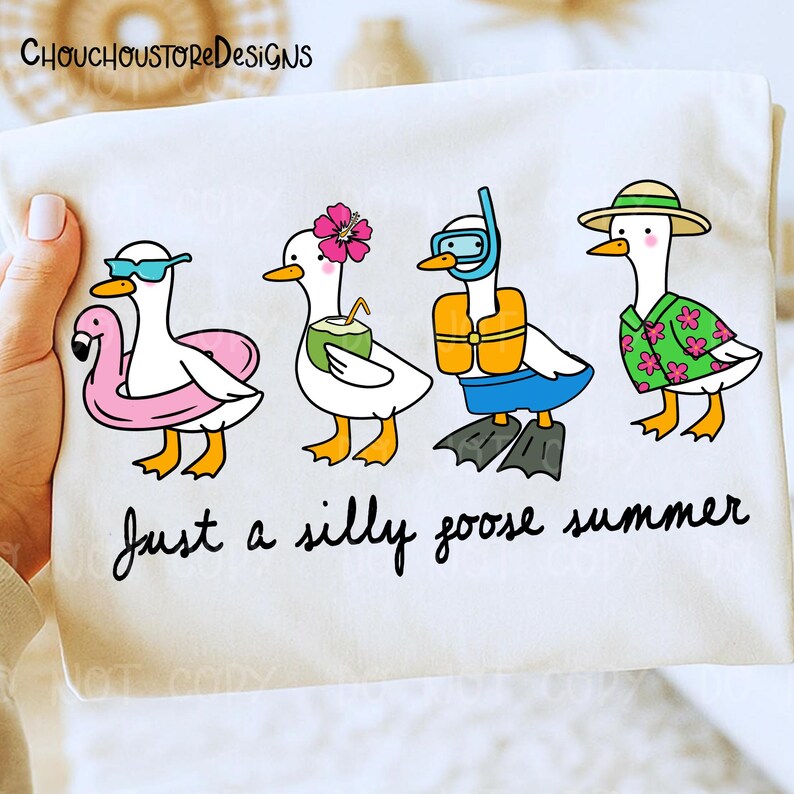 May include: White t-shirt with a whimsical illustration of four cartoon geese in summer attire. One goose wears sunglasses and a flamingo floatie, another has a flower and coconut drink, a third has a snorkel and flippers, and the last wears a hat and Hawaiian shirt. Text reads "Just a silly goose summer."