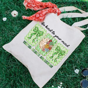 May include: A white canvas tote bag with the text "Be kind to your mind" and "Mental Health Awareness." The design includes green ribbons and a brain with flowers. A red floral scarf and sunglasses are in the background.