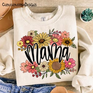 May include: Cream-colored sweatshirt with the word "Mama" in a black script font, surrounded by a colorful floral arrangement. The flowers include sunflowers, daisies, and other blooms in shades of pink, yellow, and red.