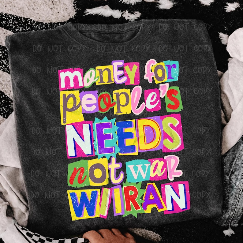 May include: Dark gray t-shirt with a colorful graphic design. The design features the words "money for people's needs not war wiran" in a variety of bright colors and fonts. The shirt is made of a soft material.