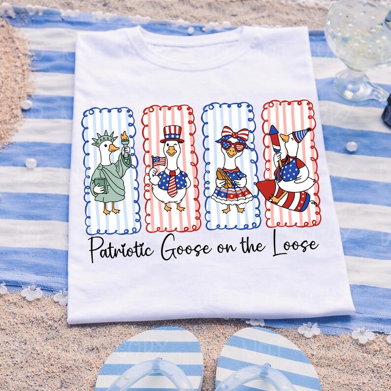 May include: White t-shirt featuring four cartoon geese dressed in patriotic attire. Each goose is framed in red and blue striped borders. The text "Patriotic Goose on the Loose" is printed below the geese. The shirt is on a blue and white striped towel.