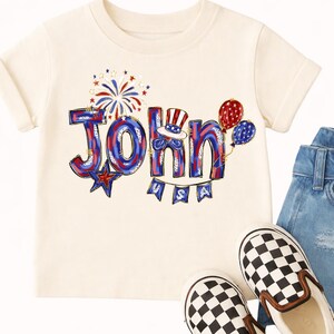 Puede incluir: Camiseta color crema con el nombre "John" en rojo, blanco y azul, decorada con fuegos artificiales, globos y una pancarta que dice "USA". La camiseta se combina con vaqueros y zapatos sin cordones a cuadros blancos y negros.