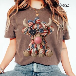 May include: Brown t-shirt featuring a patriotic Highland cow design. The cow has a bow, heart-shaped sunglasses, and is made of red, white, and blue fabric. The text "ChooHooStoreDesigns" is visible at the top.
