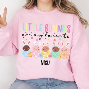 May include: Pink sweatshirt with the text "LITTLE BUNNIES are my favorite" in colorful letters. Below the text are five baby bunnies in Easter outfits, with the word "NICU" underneath.