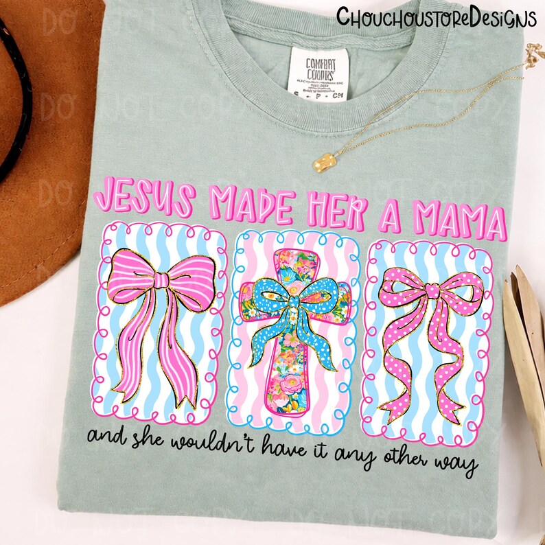 May include: Sage green t-shirt with the text "JESUS MADE HER A MAMA" in pink. The design includes three framed images of bows and a cross with floral patterns. The text "and she wouldn't have it any other way" is below the images.